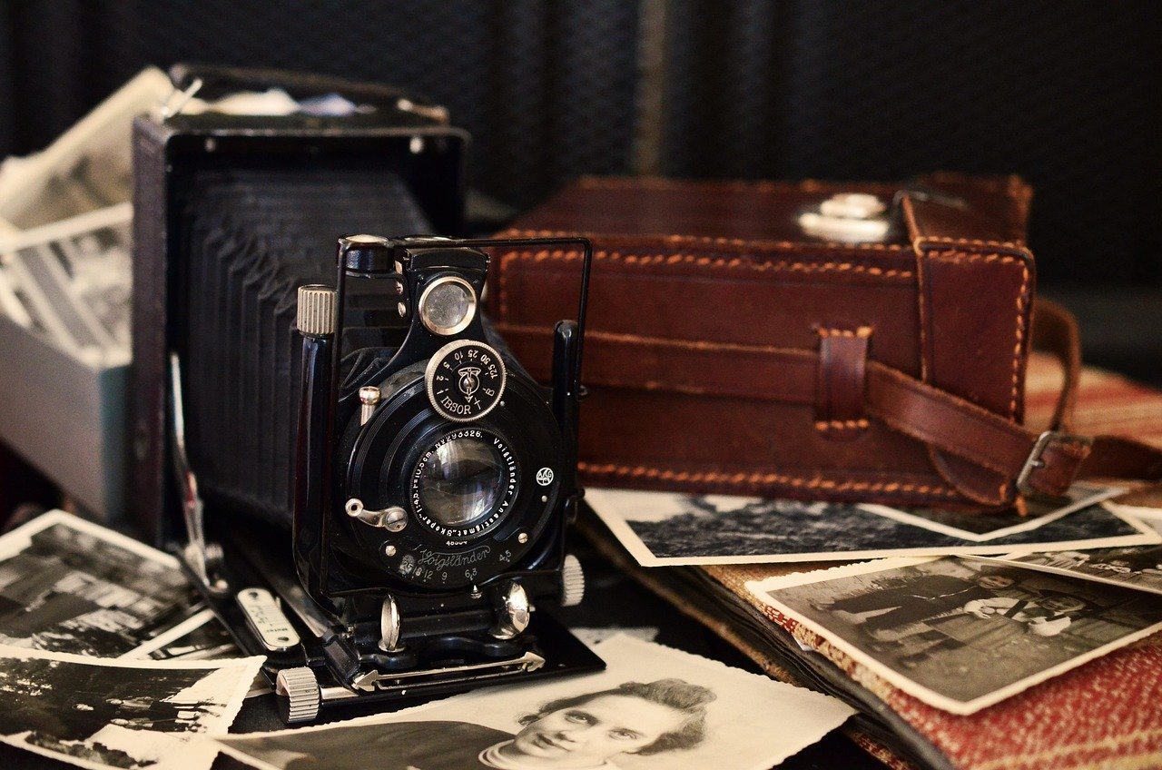 Câmera fotográfica analógica antiga entre fotografias em preto e branco e estojo de couro, representando registros visuais e a história da fotografia.